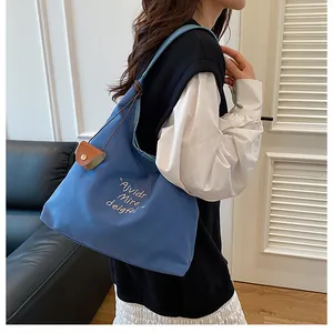 Detail of blue canvas tote bag with white lettering and brown leather accessory