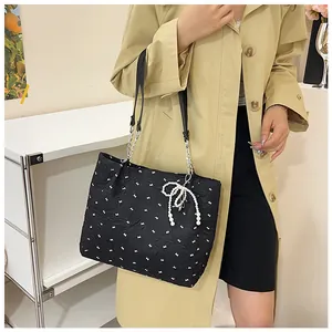Detail of black tote bag with white floral pattern, pearl bow charm and chain strap