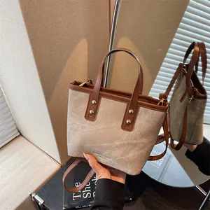 Fashionable beige canvas bucket bag with brown leather trim and metallic rivet details