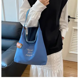 Detail of blue canvas tote bag featuring white artistic lettering and leather pendant