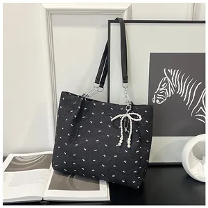 Close-up of black nylon tote bag with pearl bow charm and silver chain strap detail