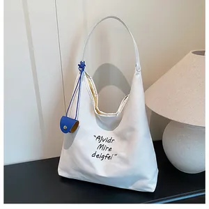 Detail of white canvas tote bag with black lettering and a blue circular charm