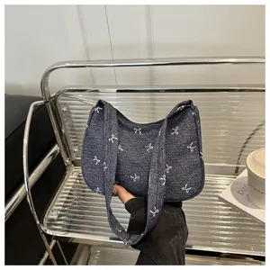 Close-up of denim underarm bag with pink bow prints and black zipper closure details