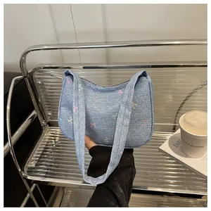 Detail of light blue denim hobo bag with colorful bow prints and metal zipper closure