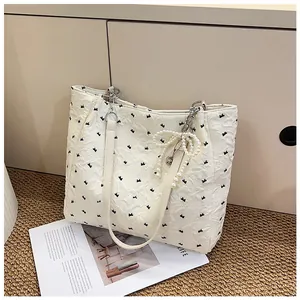 Close-up of cream tote bag with bubble texture, bow print and pearl bow charm detail