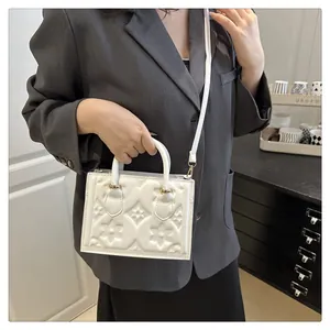 Detail of white embossed floral crossbody bag with gold hardware on a gray blazer model