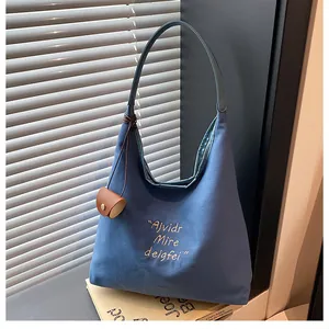 Close-up of blue canvas tote bag with white embroidery and a brown leather mini pouch