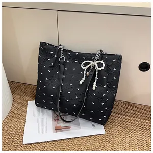 Detail of black bow-print tote bag with pearl bow pendant and metal chain shoulder strap