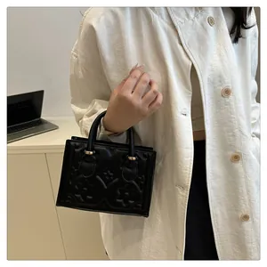 Detail of black embossed clover handbag with golden metal hardware held by a model