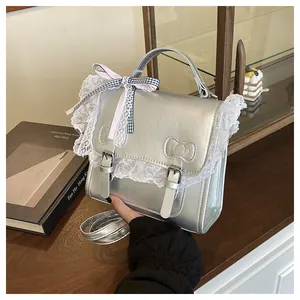 Detail of silver metallic handbag with white lace trim and bow charm held by a hand