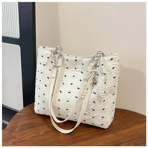 Detail of off-white tote bag with black embroidery and pearl bow charm on chain strap