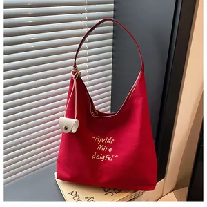 Detail of red canvas tote bag with gold embroidery and creamy white pendant charm