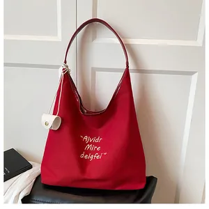 Detail of red canvas tote with white embroidery, leather strap and mini hanging pouch