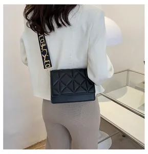 Model wearing black quilted crossbody bag with wide patterned strap for fashion styling