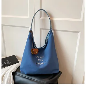 Detail of blue canvas tote bag featuring white letter embroidery and leather charms