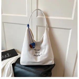 Detail of white canvas tote bag with black embroidery and blue leather pendant