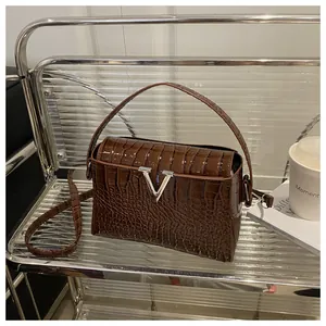 Detail of glossy brown crocodile embossed leather handbag with silver V-shaped hardware