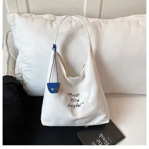 Detail of white canvas shoulder tote bag with black embroidery and blue mini pouch