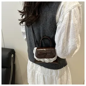 Detail of dark brown patent leather mini bag with lace trim and bow accent