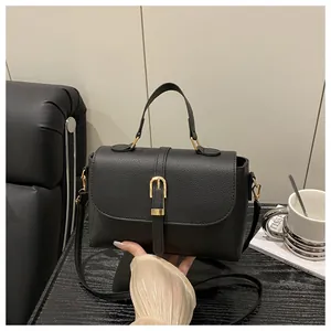 Detailed view of black litchi texture handbag with gold buckle on a stylish desk