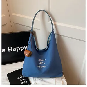 Close-up of blue textured canvas tote bag with white embroidery and brown leather coin pouch