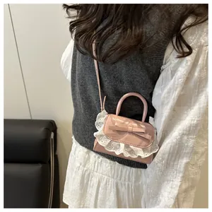 Detail of pink mini bow bag featuring lace trim and glossy finish on model