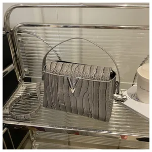 Detail of grey crocodile texture leather bag with silver V-shaped metal hardware