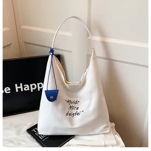 Detail of white canvas tote bag with black embroidery and blue coin purse charm