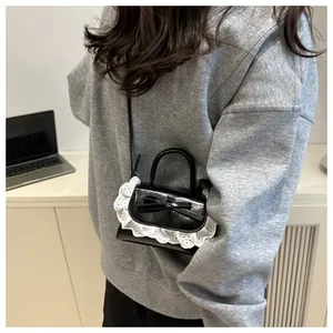 Close-up of mini black leather bag with sweet bow and white lace trim detail