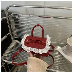 Detail of red patent leather mini bag with lace trim and bow on silver background