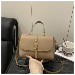 Detail view of khaki pebbled leather handbag with gold buckle and top handle