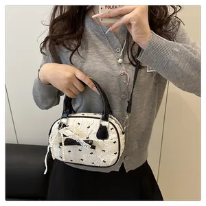 Close-up of white crossbody bag with black bow patterns and pearl lace charm detail