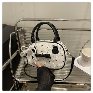 Detail of white wrinkled handbag with black bow patterns and pearl charm on a rack