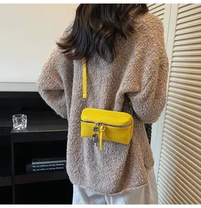 Detail of yellow PU leather crossbody bag with metal charm on a cozy model backdrop