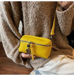 Detail of a bright yellow crossbody bag with silver robot charm and zipper texture