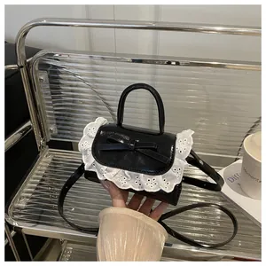 Close-up of black glossy mini crossbody bag featuring white lace edges and a bow