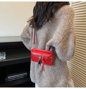 Red crossbody bag with silver robot charm shown on a beige sweater background