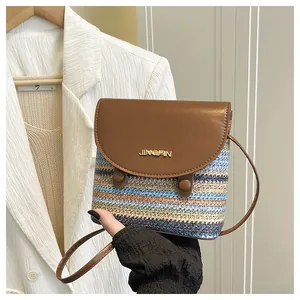 Detail of colorful woven straw bucket bag with brown leather flap and golden logo