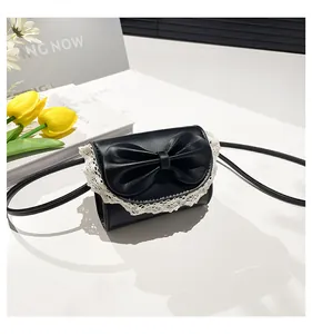 Detail of mini black crossbody bag with large bow and white lace trim decoration