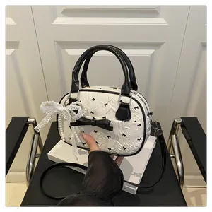 Detail view of white Boston bag featuring black bow patterns and lace pearl charm