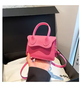 Macro shot of a pink mini crossbody bag in pebble grain leather held by hand