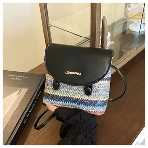 Detail of a woven rainbow straw bag featuring a black leather flap and gold logo