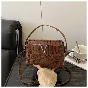 Detail of a brown crocodile texture handbag featuring a silver V-shaped metal logo
