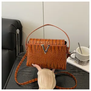 Detail of luxury brown crocodile textured handbag with silver V-shaped metal logo