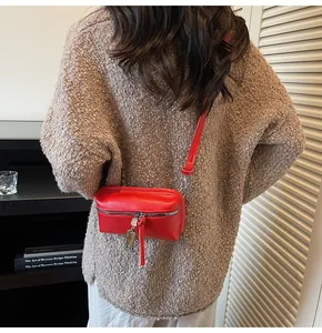 Detail of red faux leather crossbody bag with silver zipper and robot charm accessory