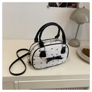 Close-up of white boston bag with black bow print and leather handles in a cozy setting