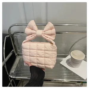 Detail of light pink quilted puff handbag featuring a large bow handle and gold metal zipper