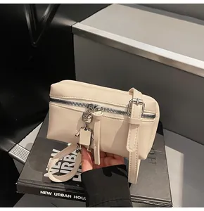 Close-up of minimalist beige square bag with silver robot charm on black books