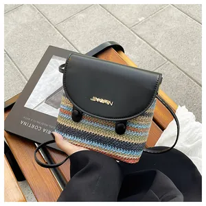 Detail of colorful woven straw bucket bag with black leather flap and metal logo