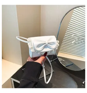 Close-up of a white mini flap bag with a large bow detail and delicate lace trim edge